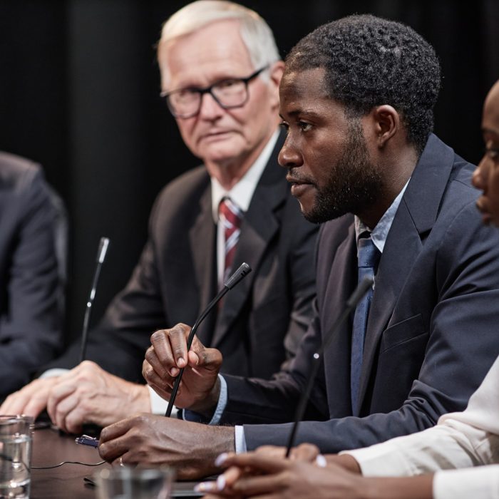Side view of high profile African American politician speaking into microphone reporting on reform plans while sitting in line with other officials during press conference, copy space